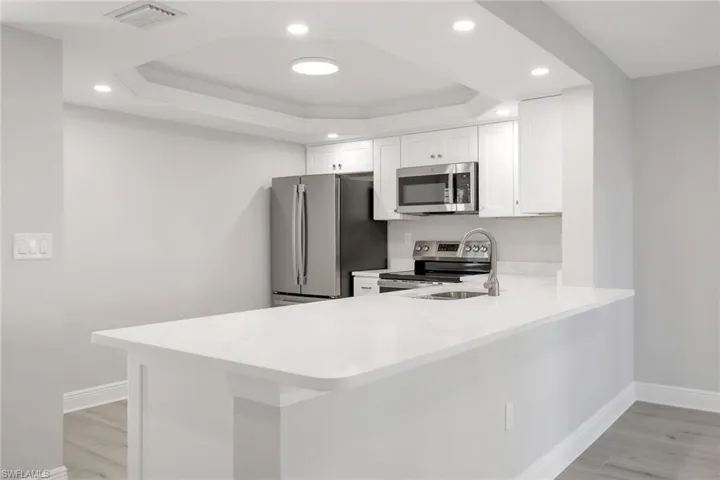 Kitchen with white cabinetry, a tray ceiling, and kitchen peninsula large enough for 4 stools