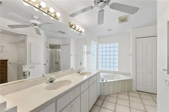 Bathroom featuring double sink vanity, tile patterned flooring, ceiling fan, and separate shower and tub