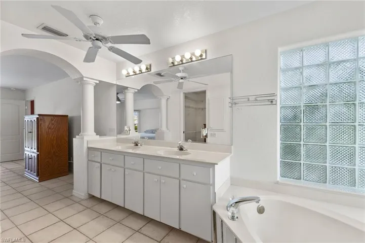 Bathroom featuring decorative columns, ceiling fan, plenty of natural light, tile patterned flooring, and a tub to relax in