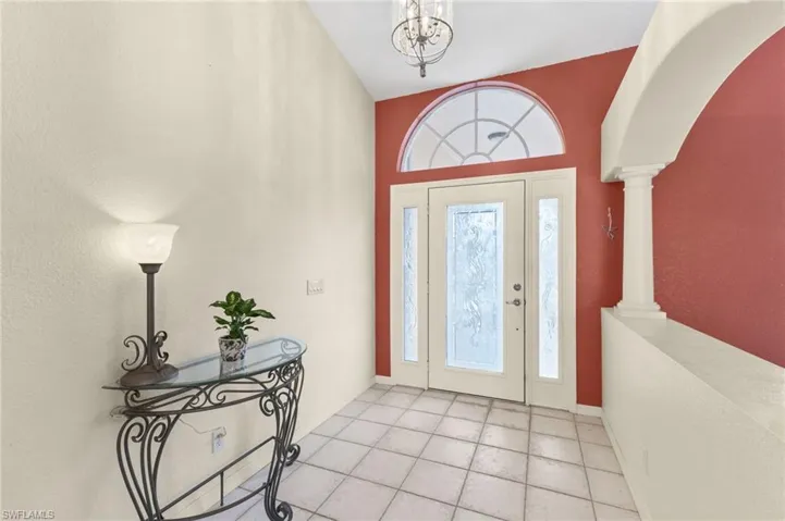 Foyer entrance with light tile patterned floors, a notable chandelier, ornate columns, and plenty of natural light