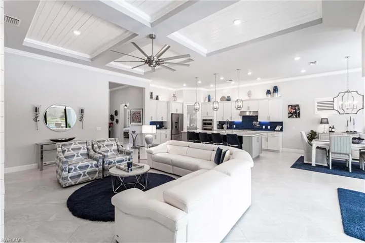 Living room featuring coffered ceiling, ceiling fan with notable chandelier, sink, ornamental molding, and beamed ceiling