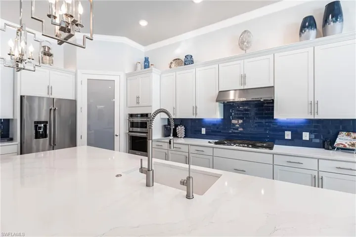 Kitchen featuring stainless steel appliances, white cabinetry, hanging light fixtures, and light stone counters