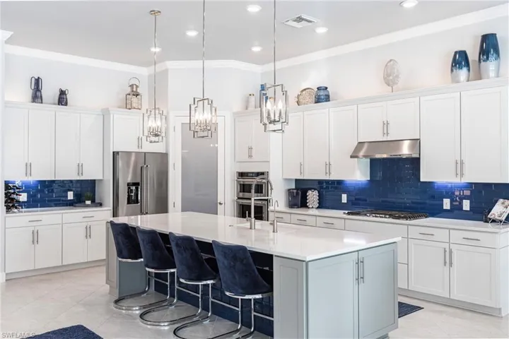 Kitchen featuring a kitchen bar, stainless steel appliances, a kitchen island with sink, pendant lighting, and white cabinetry