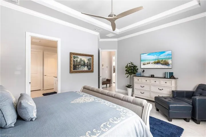 Bedroom with connected bathroom, a tray ceiling, ceiling fan, and ornamental molding