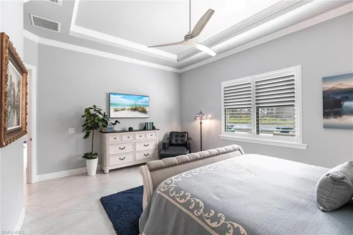 Tiled bedroom with a tray ceiling, ceiling fan, and crown molding