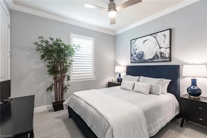 Carpeted bedroom featuring ceiling fan and crown molding