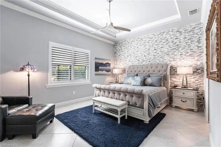 Bedroom featuring light tile patterned floors, a tray ceiling, ceiling fan, and crown molding