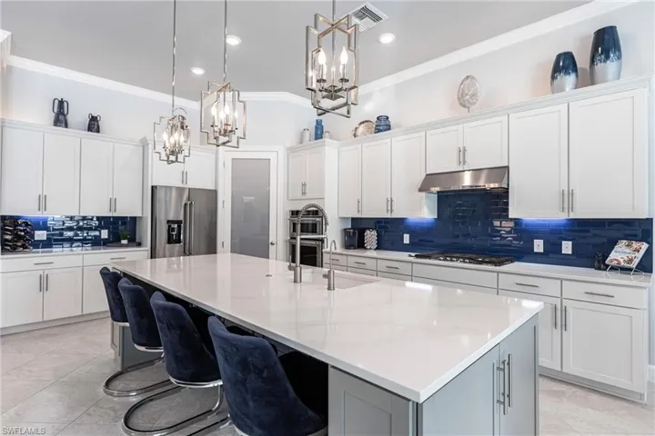 Kitchen with white cabinets, appliances with stainless steel finishes, decorative light fixtures, and a spacious island