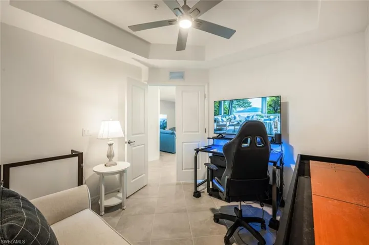 Office space with light tile patterned floors, visible vents, ceiling fan, and a tray ceiling