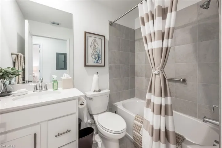 Full bathroom with visible vents, toilet, electric panel, shower / tub combo, and vanity