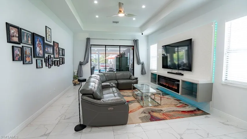 Living space featuring tray ceiling with recessed lighting, porcelain tile flooring, built-in entertainment center with electric fireplace, and sliding glass doors to the exterior