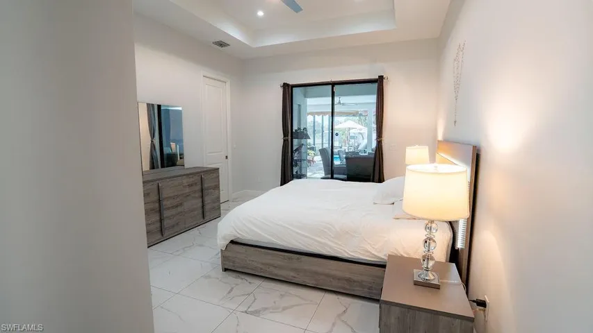 Bedroom featuring marble-look tile flooring, a tray ceiling with recessed lighting, and a ceiling fan