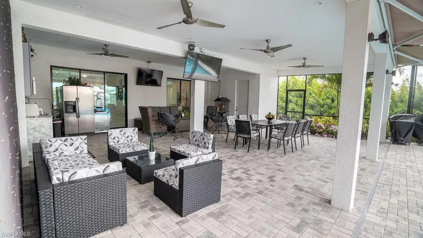 Covered outdoor patio featuring brick paver flooring, multiple ceiling fans, recessed lighting, and a built-in outdoor kitchen area with a stainless steel refrigerator