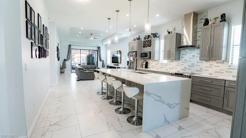Contemporary kitchen featuring an oversized island with waterfall countertop, pendant lighting, stainless steel appliances, and grey cabinetry