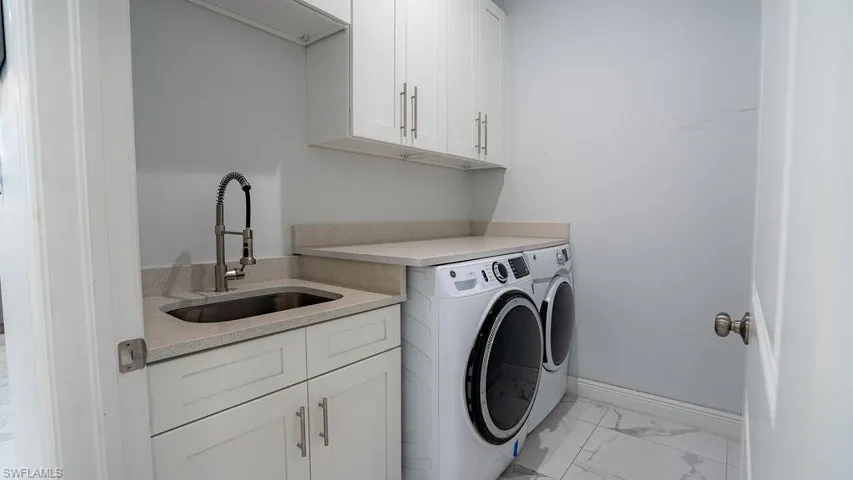 Laundry area featuring a built-in utility sink, light-toned countertop, white cabinetry with brushed nickel hardware, and marble-look tile flooring