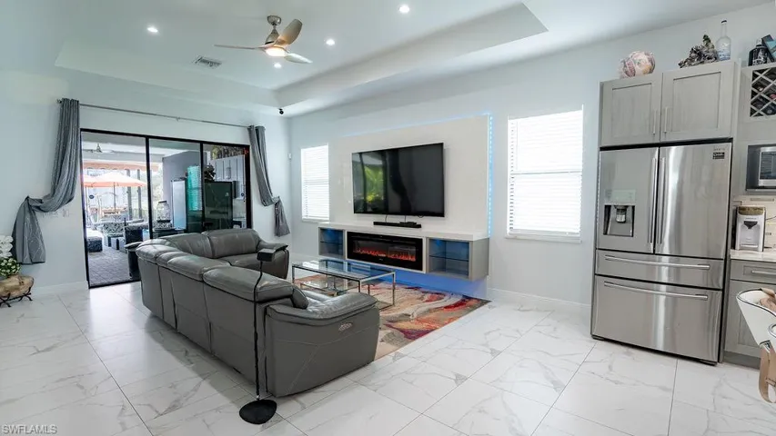 Open-concept living space with large format tile flooring, a tray ceiling, recessed lighting, and a contemporary ceiling fan