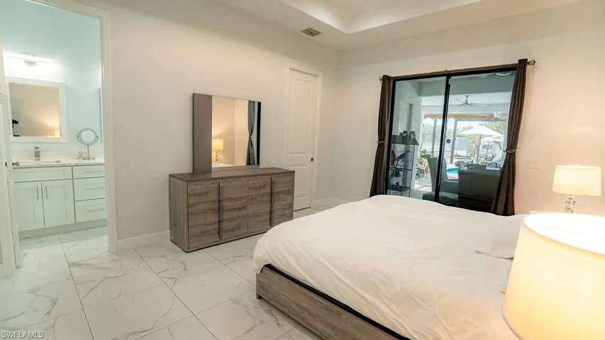 Bedroom featuring large format tile flooring, a tray ceiling, and sliding glass doors leading to an outdoor living area