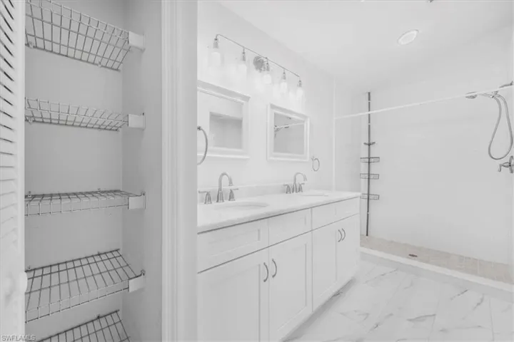 Full bath with double vanity, linen closet, light tile finish flooring with tiled shower.