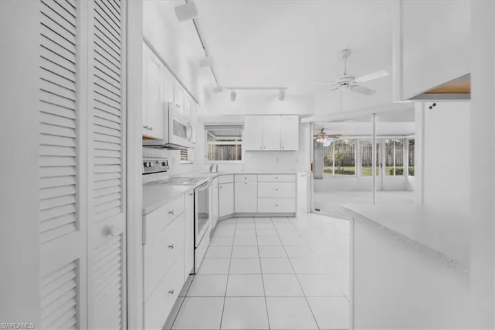 Kitchen featuring white appliances, quartz countertops, pantry & tiled flooring.
