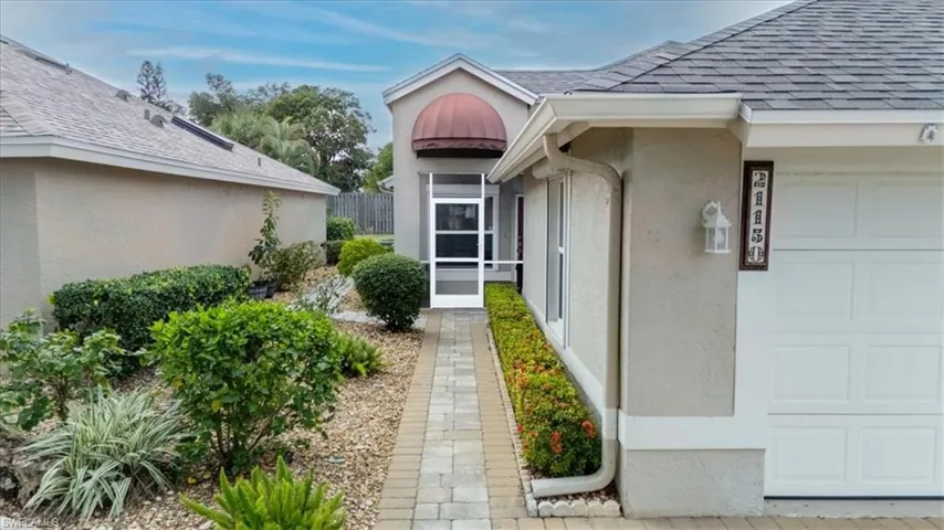 Property entrance with a shingled roof, stucco siding, a garage, and a sunroom