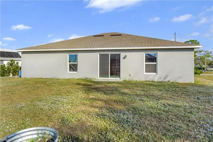 Back of property featuring a shingled roof, a lawn, and stucco siding