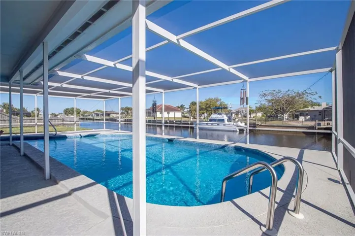 Outdoor pool featuring glass enclosure, a water view, a patio, and a dock