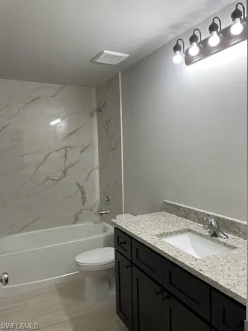 Full bathroom with vanity, tile patterned flooring, tiled shower / bath combo, and toilet