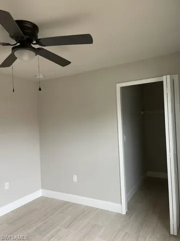 Unfurnished bedroom featuring a walk in closet, ceiling fan, light hardwood / wood-style floors, and a closet