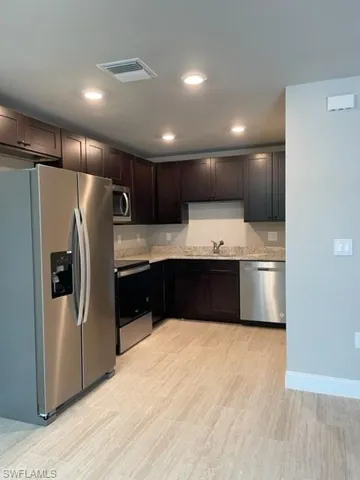 Kitchen with range, dark brown cabinets, dishwasher, fridge, and sink