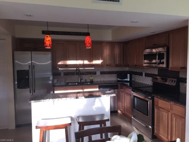Kitchen featuring appliances with stainless steel finishes, decorative light fixtures, dark stone counters, a breakfast bar area, and tasteful backsplash