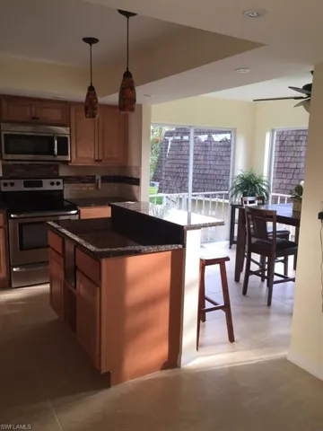 Kitchen featuring stainless steel appliances, decorative backsplash, dark stone countertops, decorative light fixtures, and a breakfast bar area