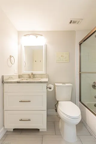Full bathroom featuring toilet, baseboards, vanity, and enclosed tub / shower combo