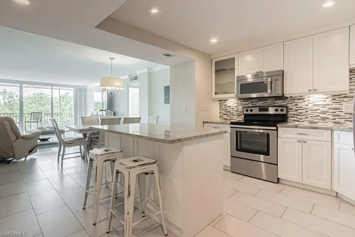 Kitchen featuring stainless steel appliances, tasteful backsplash, light stone countertops, open floor plan, and a kitchen breakfast bar