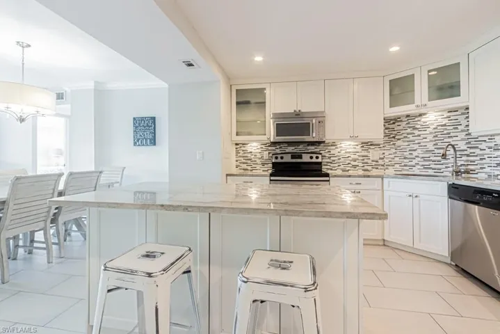 Kitchen with stainless steel appliances, a sink, decorative backsplash, a breakfast bar, and light stone countertops