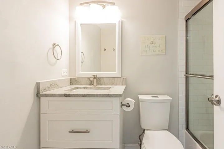 Full bath with toilet, vanity, and shower / bath combination with glass door