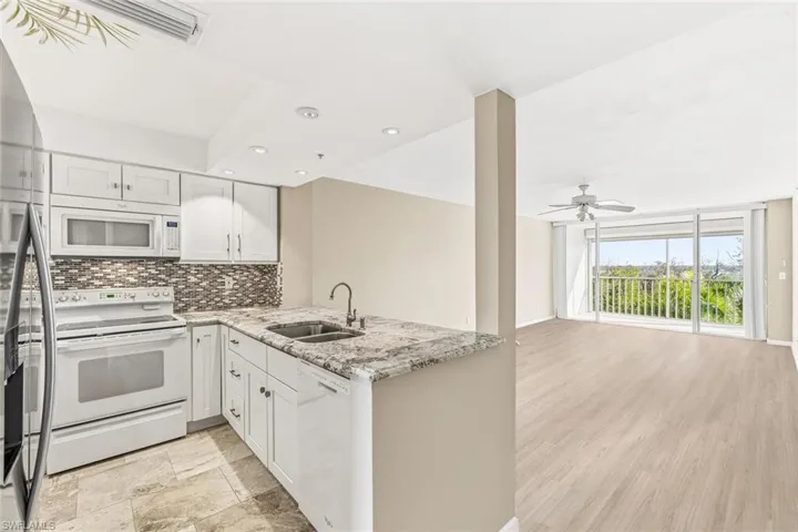 Kitchen featuring white appliances, light stone countertops, white cabinets, open floor plan, and a peninsula