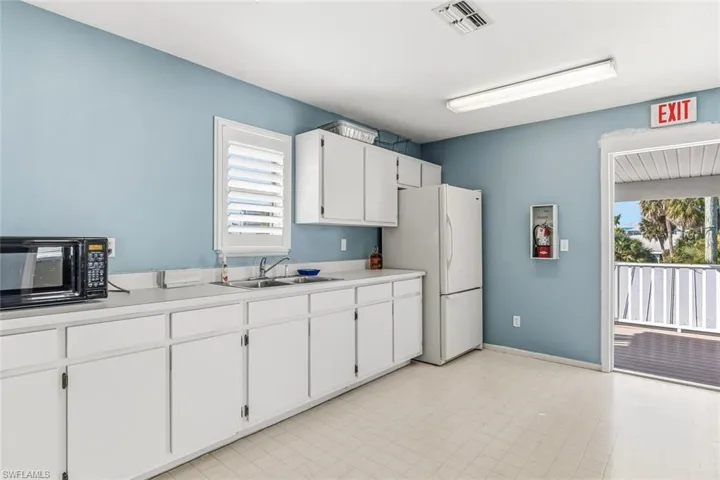 Kitchen with white cabinets, light countertops, black microwave, and freestanding refrigerator