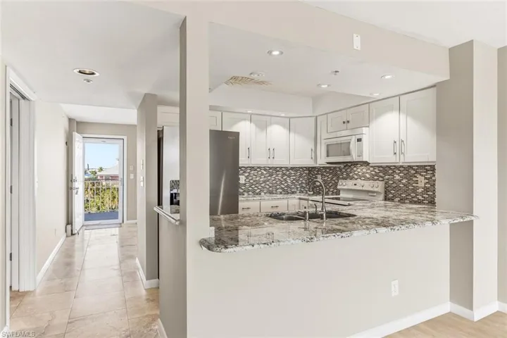 Kitchen featuring white appliances, white cabinetry, light stone countertops, tasteful backsplash, and recessed lighting