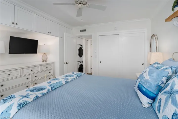 Bedroom featuring ceiling fan, stacked washer and dryer, ornamental molding, and a closet
