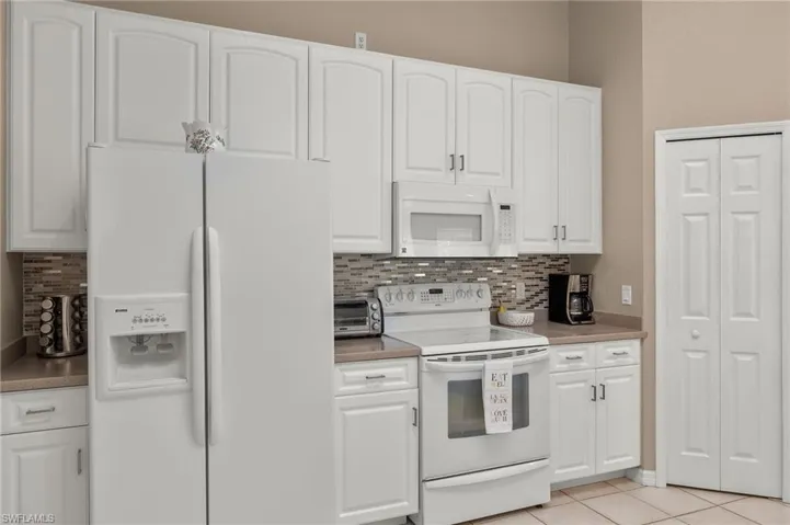 Kitchen with white cabinetry, light tile patterned flooring, and white appliances