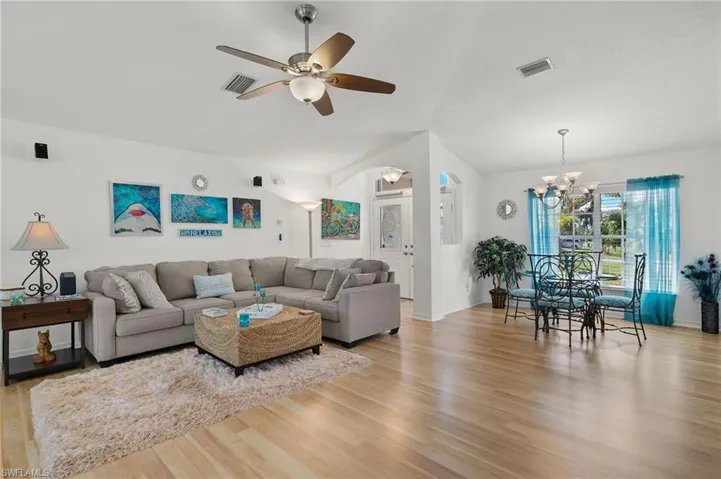 Living room featuring ceiling fan with notable chandelier and light wood-type flooring