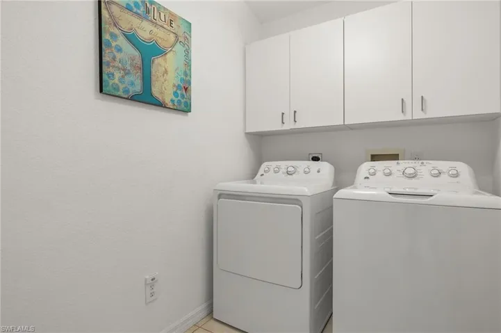 Washroom with light tile patterned flooring, washing machine and clothes dryer, and cabinets