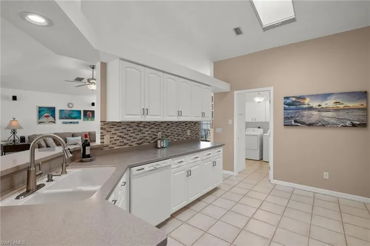 Kitchen featuring light tile patterned floors, white cabinetry, washer and dryer, white dishwasher, and sink