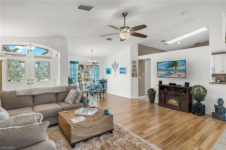 Living room featuring light hardwood / wood-style floors, lofted ceiling, french doors, and ceiling fan with notable chandelier