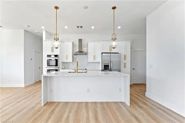 Kitchen with white cabinets, light stone countertops, a kitchen island with sink, stainless steel appliances, and light wood-type flooring