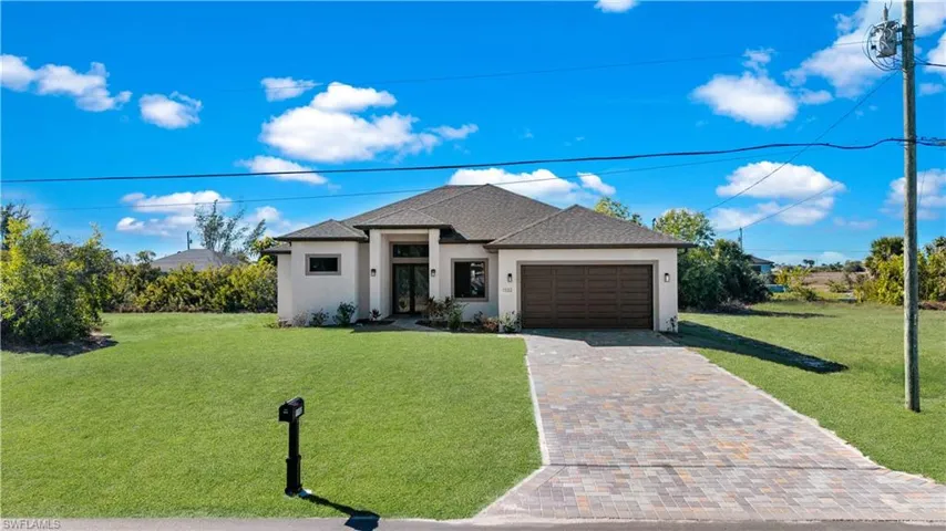 View of front facade with a front lawn, stucco siding, a garage, driveway, and roof with shingles