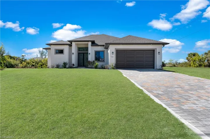 Prairie-style house featuring a front yard, stucco siding, decorative driveway, an attached garage, and roof with shingles
