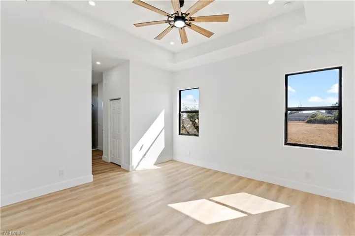 Unfurnished room with light wood-type flooring, recessed lighting, ceiling fan, and a raised ceiling