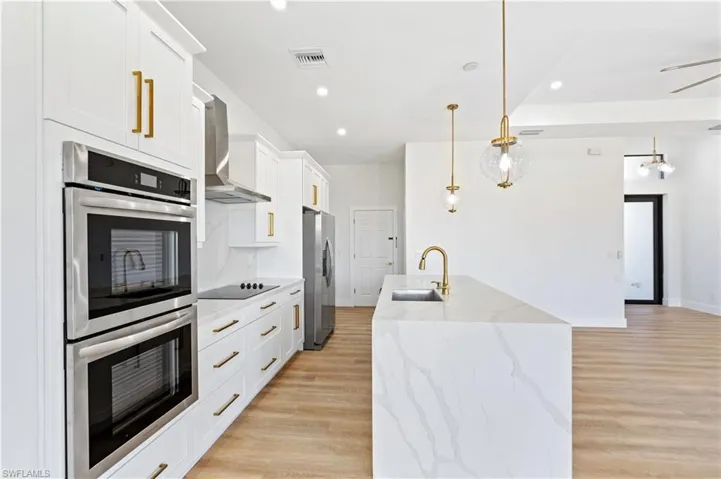 Kitchen with stainless steel appliances, light stone countertops, pendant lighting, and light wood-type flooring