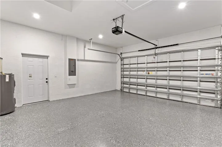 Garage featuring electric water heater, electric panel, a garage door opener, and recessed lighting